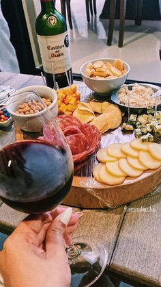 a person holding a wine glass in front of a table full of cheeses and crackers