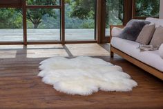 a white sheepskin rug on the floor in front of a couch and large windows