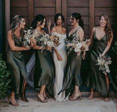 a group of women standing next to each other in front of a wooden door holding bouquets