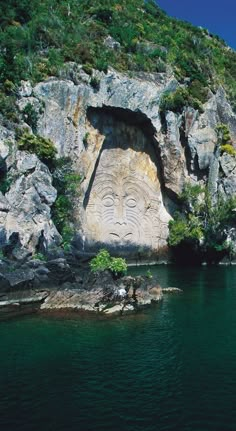 a large face carved into the side of a cliff next to a body of water