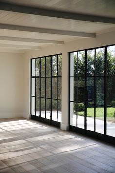 an empty room with large windows and wood flooring in the center, looking out onto a yard