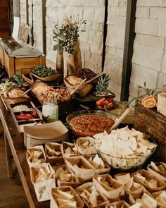 a table filled with lots of food on top of a wooden table next to a brick wall