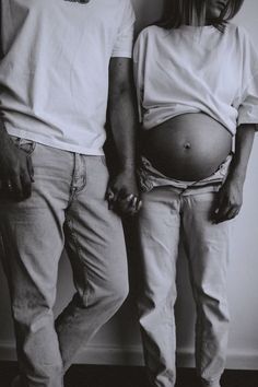 a man and woman standing next to each other in front of a wall holding hands