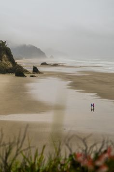 two people are walking on the beach in the fog