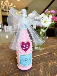 a pink bottle with a heart on it sitting on a table next to some flowers