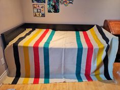 a bed covered in a multicolored blanket next to a wall with pictures on it