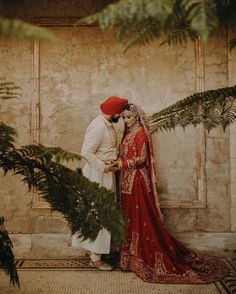 a bride and groom standing next to each other in front of a wall with greenery