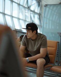 a young man sitting on top of an airport bench next to a brown leather chair