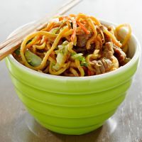 a green bowl filled with noodles and meat next to chopsticks on a table