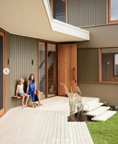 two children sitting on the porch of a house with wooden steps and grass in front of them