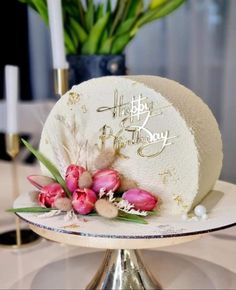 a white cake with pink flowers on top and happy birthday written on the side in gold lettering