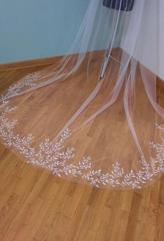 a wedding veil with white flowers and leaves on the bottom is laying on top of a wooden floor