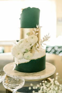 a three tiered cake with white flowers and greenery on the top is sitting on a table