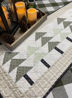 a quilted table runner with pine cones and candles on it next to a candle holder