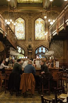 people are sitting at tables in an old fashioned restaurant with stained glass windows and chandeliers