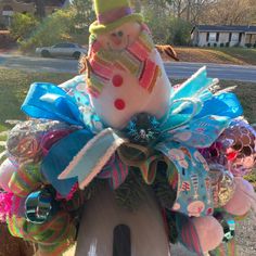 a snowman sitting on top of a birdhouse decorated with ribbons and bows,