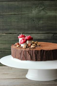 there is a chocolate cake with nuts and berries on top, sitting on a white plate