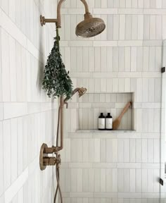 a bathroom with white tiled walls and flooring, including a shower head and hand held faucet