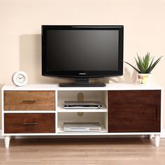 a flat screen tv sitting on top of a white entertainment center next to a potted plant