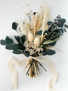 an arrangement of dried flowers and greenery on a white background with a ribbon tied around it