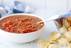 a white bowl filled with salsa next to tortilla chips and a bag of chips