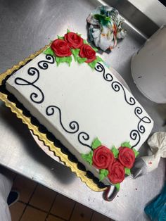 a decorated cake sitting on top of a metal counter next to a white plate with red roses