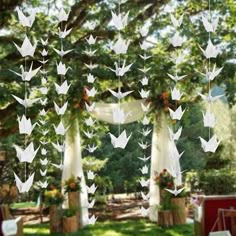 an outdoor wedding with paper cranes hanging from the ceiling and flowers in vases on the ground