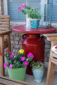 a red table with flowers on it and two chairs in front of it, next to a potted plant