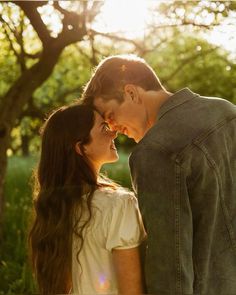 a young man and woman standing next to each other in the grass with trees behind them