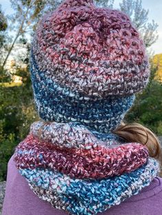 a woman wearing a multicolored knitted hat and neck scarf in front of trees