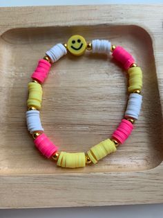 a yellow smiley face beaded bracelet with pink, white and yellow beads on a wooden tray