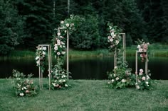 an outdoor ceremony setup with flowers and greenery on the grass near a body of water