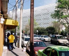 several cars parked on the side of a street next to a tall building with a white perfored roof