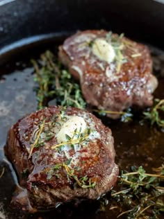 two steaks cooking in a skillet with herbs