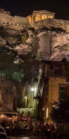 an old city street at night with cars parked on the side and people walking around