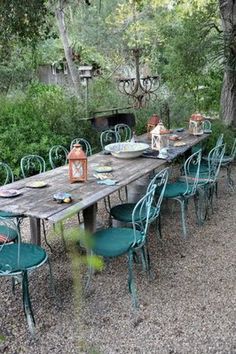 an outdoor table and chairs set up in the middle of a gravel area surrounded by trees