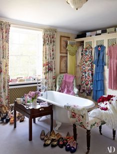 a bath tub sitting next to a window in a bathroom filled with shoes and dresses