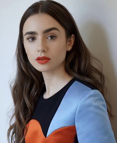 a woman with long brown hair wearing an orange and blue dress is looking at the camera