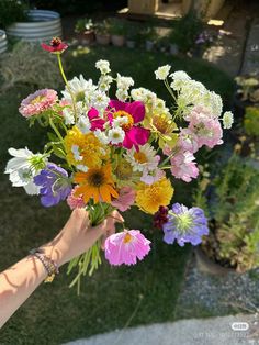 a person holding a bouquet of flowers in their hand on the grass near some plants