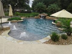 an outdoor pool with waterfall and umbrellas next to it in the middle of a yard