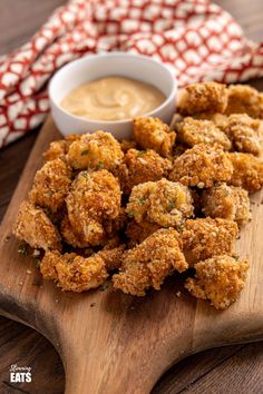 some fried food on a wooden cutting board next to a bowl of dip and napkin