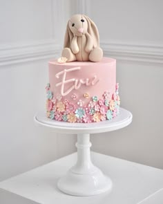 a pink cake decorated with flowers and a bunny on top