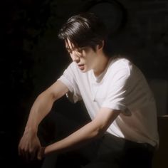 a young man sitting on top of a wooden bench next to a tree in the dark