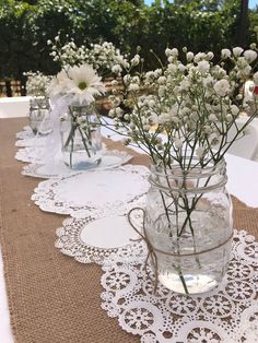 white flowers are in mason jars with lace doily on a table cloth at an outdoor wedding