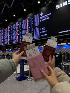 two people holding up their passport in front of an electronic screen at an airport terminal