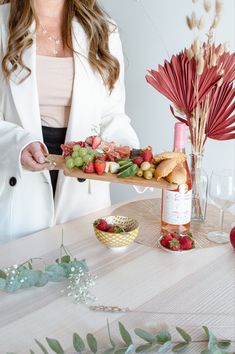 a woman holding a tray with fruit and bread on it next to a bottle of wine