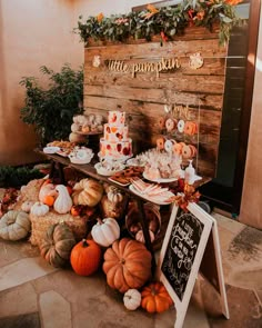 a table filled with lots of pumpkins next to a wooden sign that says,