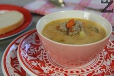 a bowl of soup on a red and white plate next to a slice of bread