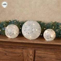 three glass balls sitting on top of a mantle next to a christmas tree with lights