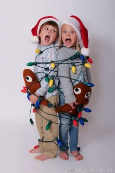 two children wearing christmas lights and santa hats, standing next to each other with their mouths open